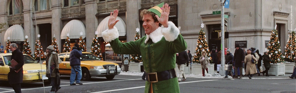 An elf prances through a busy New York Street, his hands held up