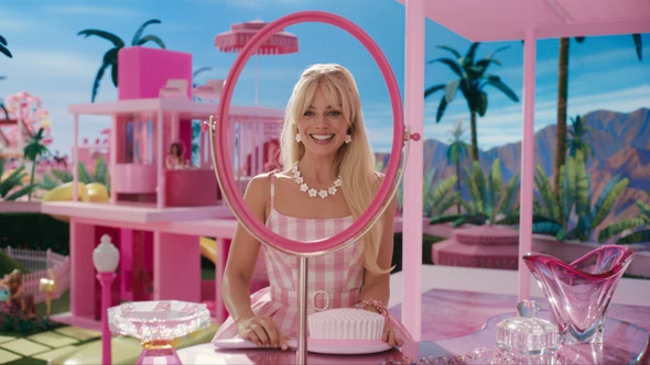 Barbie (played by Margot Robbie) smiles at her perfect reflection in the perfect Barbie world. This film is covered by our Blanket Licence for ambient screenings.