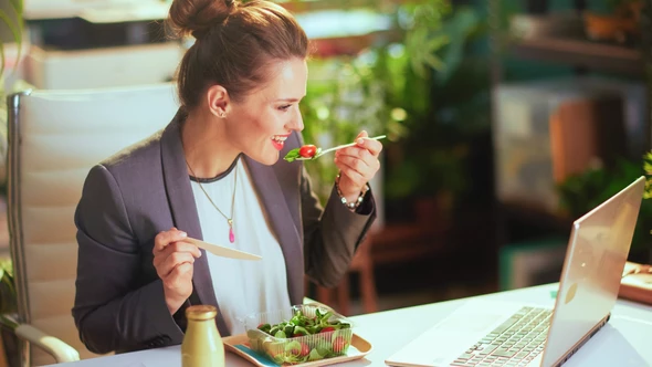 A lady is eating lunch at her desk at work while watching a film or a TV series - covered by the Filmbankmedia Blanket Licence