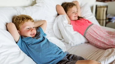 Two children are enjoying watching a film on the hotel bed