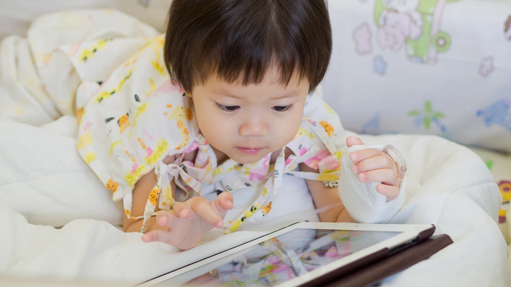 A little girl with a broken wrist is watching a film on her tablet on her hospital bed