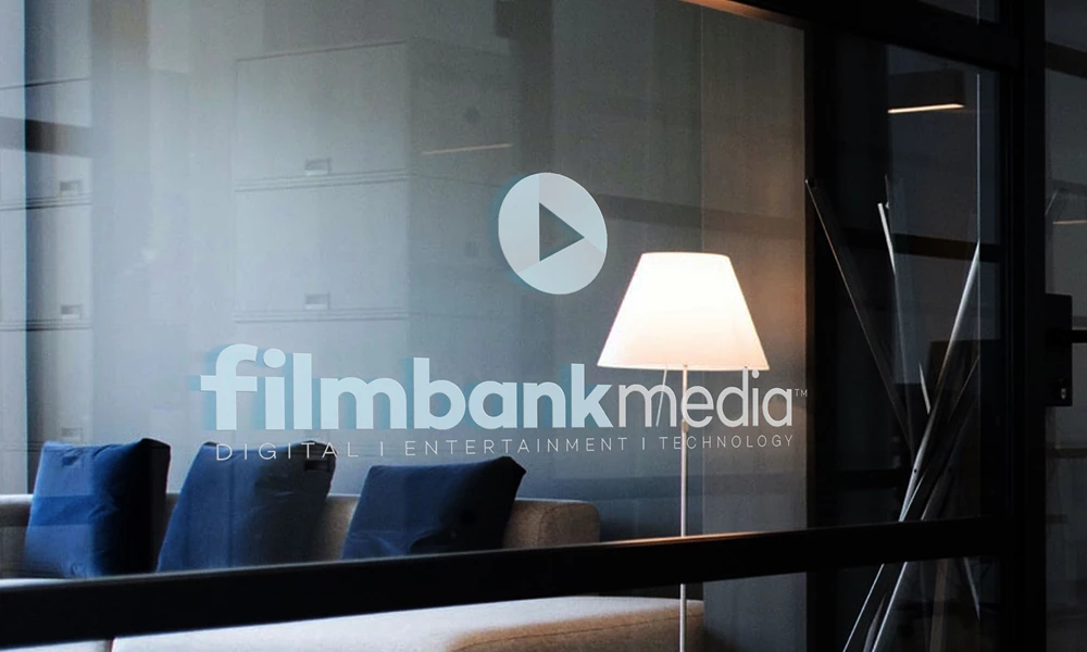 An office glass interior wall features the Filmbankmedia branding. A lamp is pictured in the background.