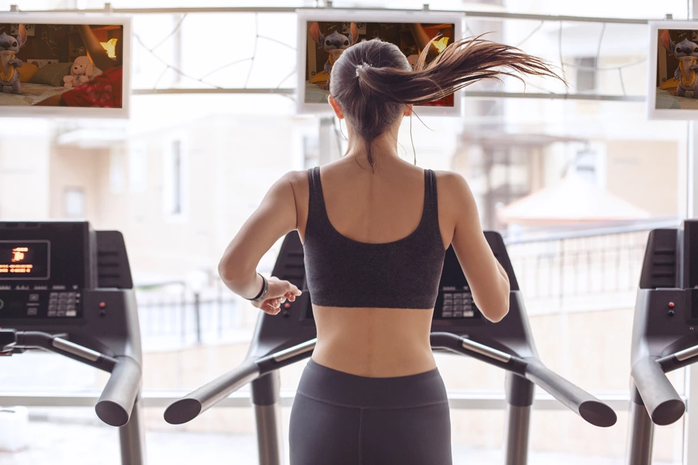 Lady running on a treadmill at the gym, watching Lilo & Stitch on a screen