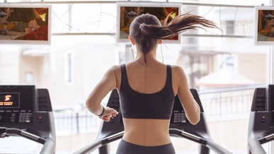 A lady is running on a threadmill at the gym while Lilo & Stitch is showing on TV screens around the gym