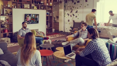 Employees are relaxing in a staff room while The Big Bang Theory is showing on a TV screen on the wall