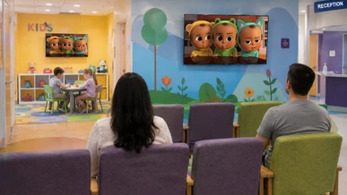 Two children are playing in kids corner in the waiting room of a hospital while Baby Boss is showing on TV screens on the wall